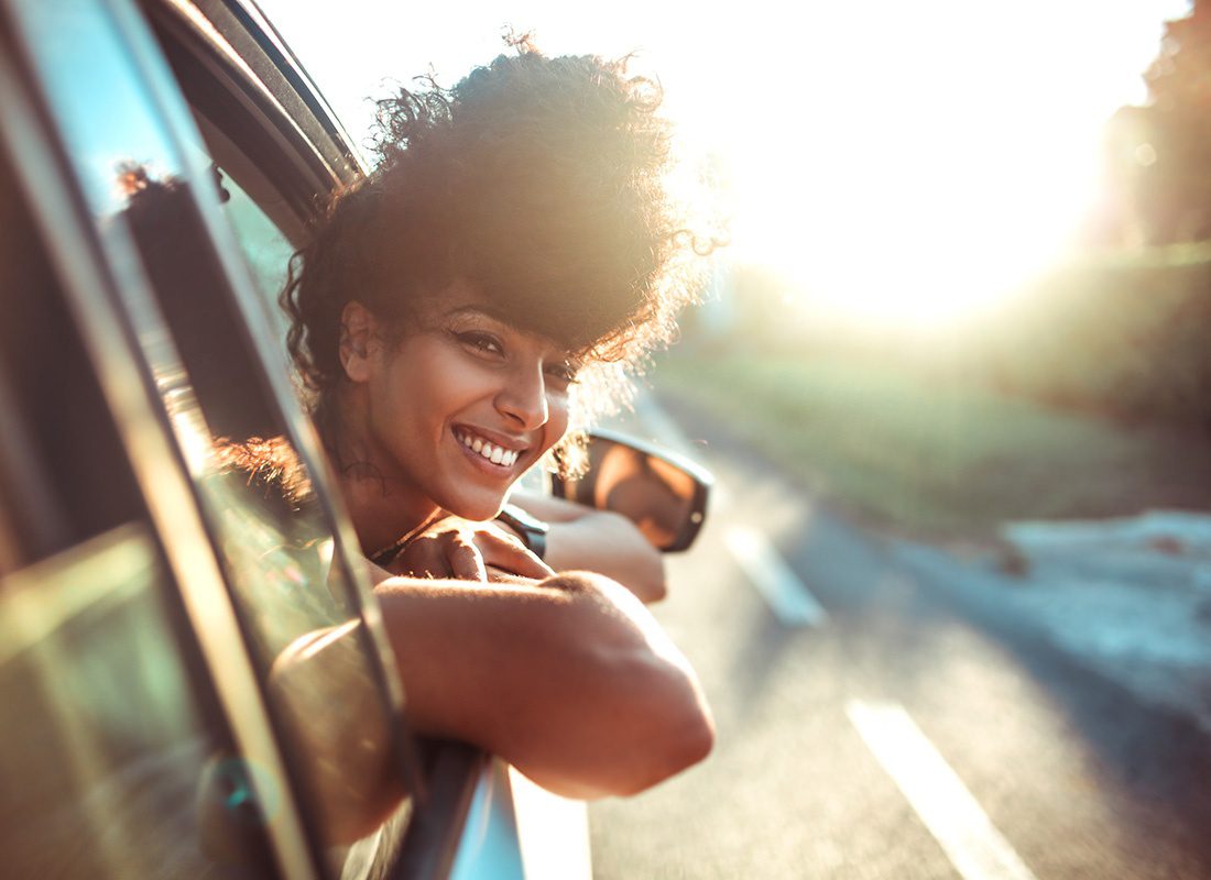 Contact - Closeup Portrait of a Smiling Young Woman Riding in a Car on a Sunny Day Sticking her Head Out of the Window to Look Around