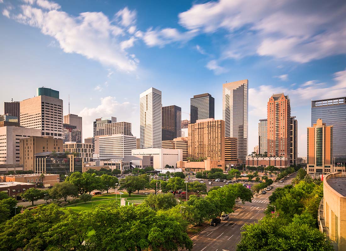 Houston, TX - View of Modern Buildings with a Park Full of Green Trees Out Front Against a Cloudy Blue Sky in Houston Texas