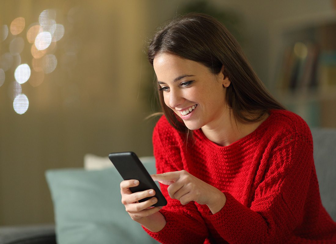 Video Library - Woman Smiling and Looking at Her Phone While Sitting at Her Home in the Afternoon